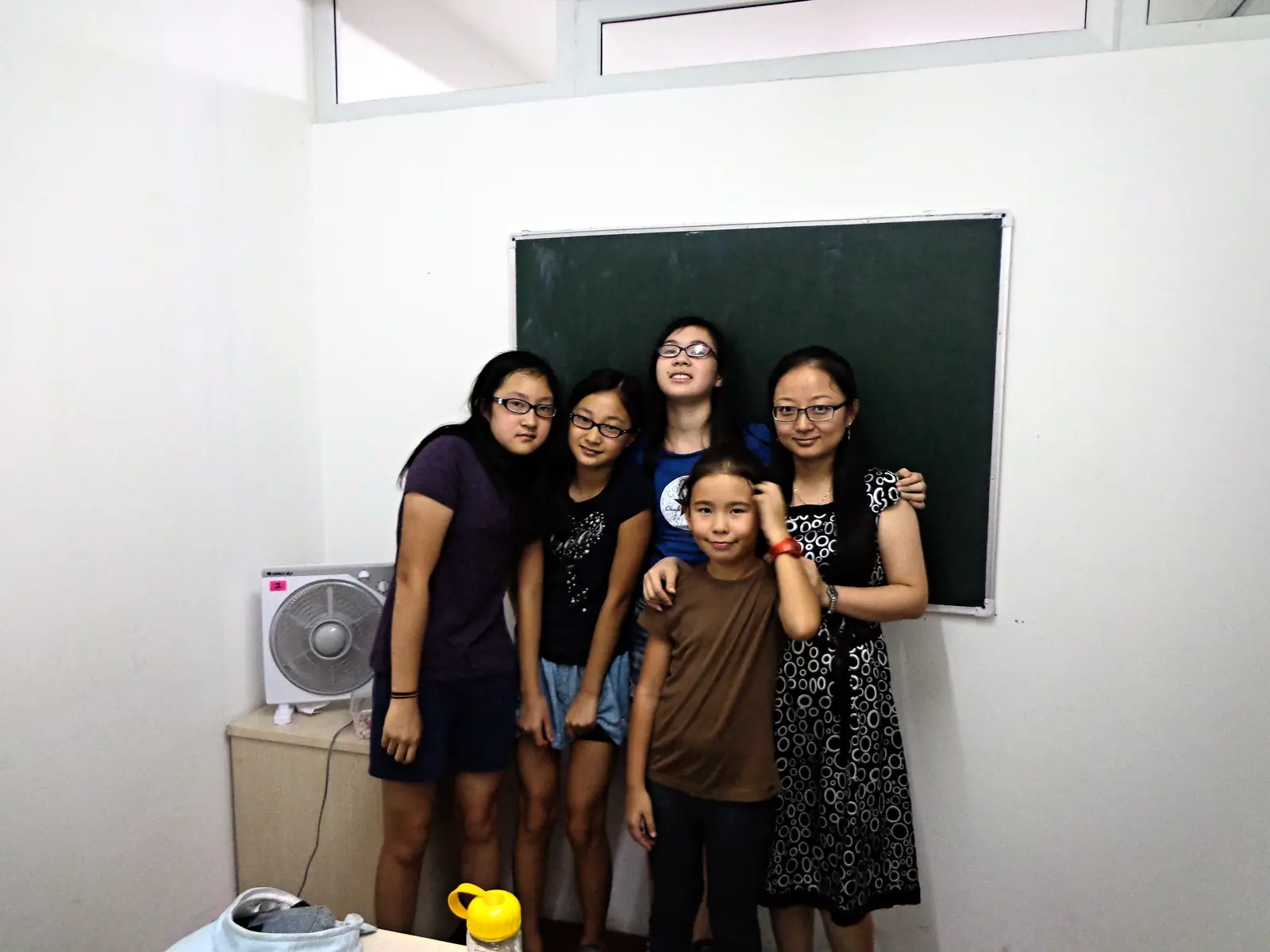 Five teenage students together in front of a classroom blackboard