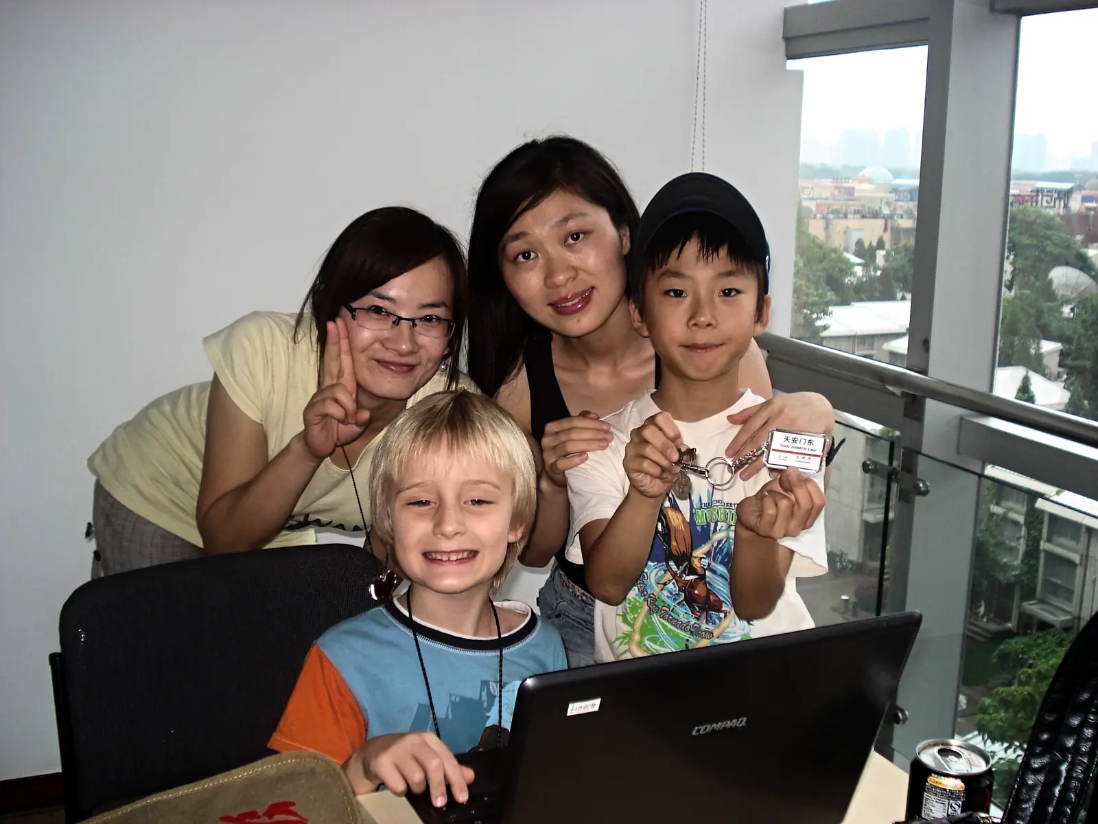 Two teachers and two young students gathered around a laptop, the city visible through the window