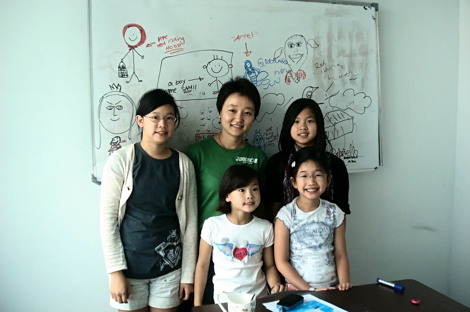 A teacher with four young students in front of a whiteboard covered in their own classwork