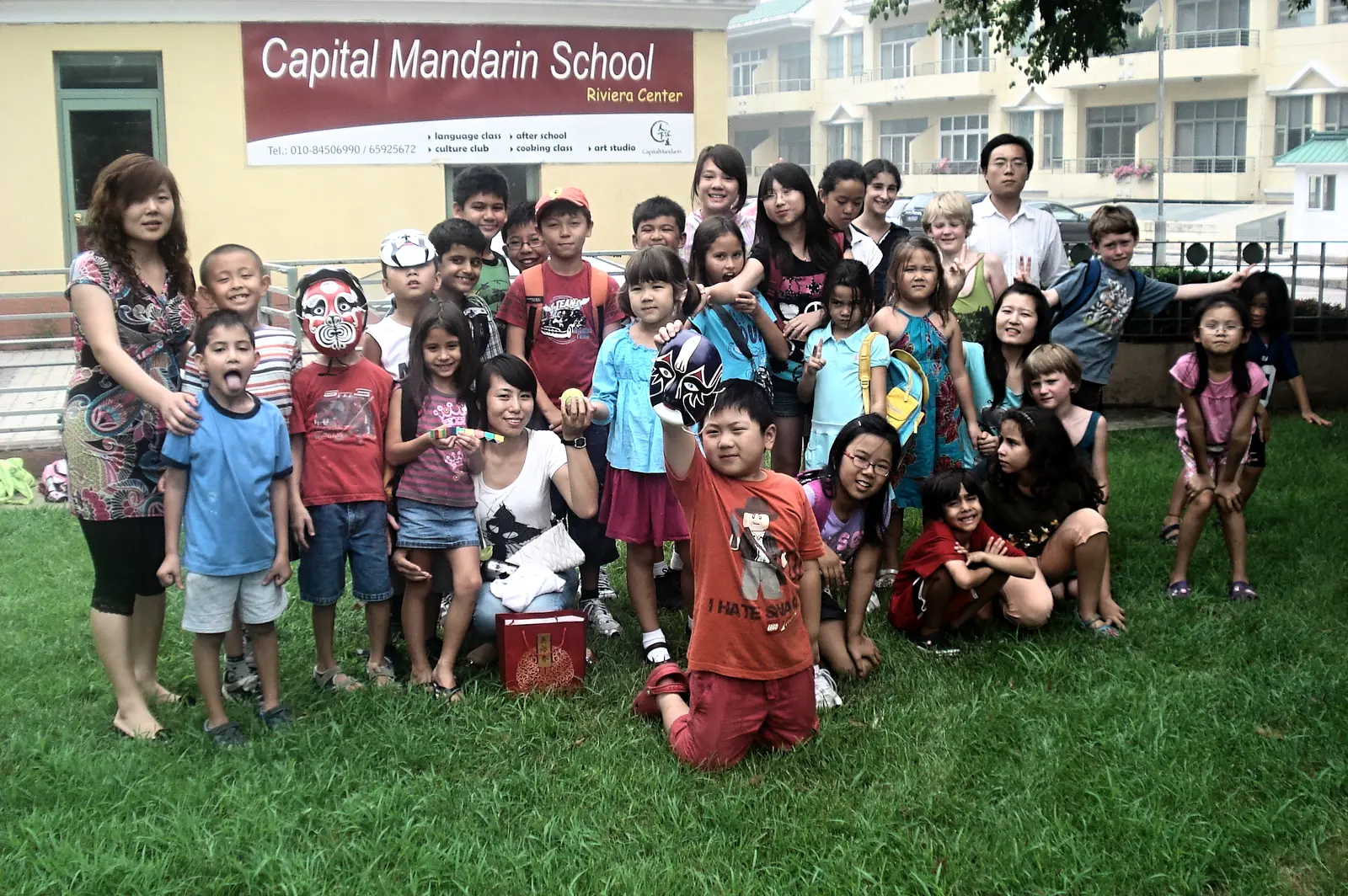 A large group of children and teachers on the lawn beneath the school's sign