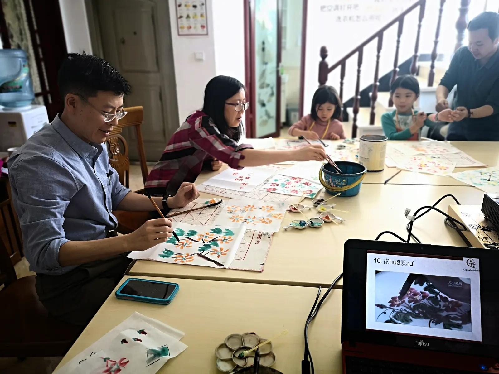 A guided ink-painting workshop around a long table, students painting flowers