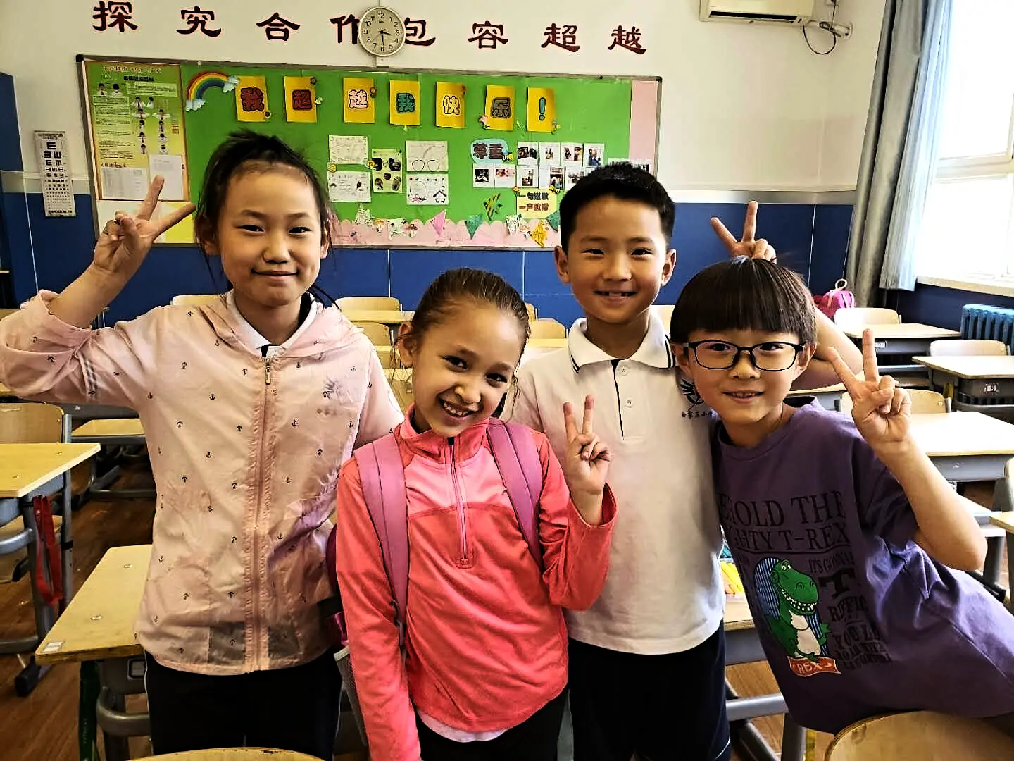 Four classmates grinning at the camera in their classroom