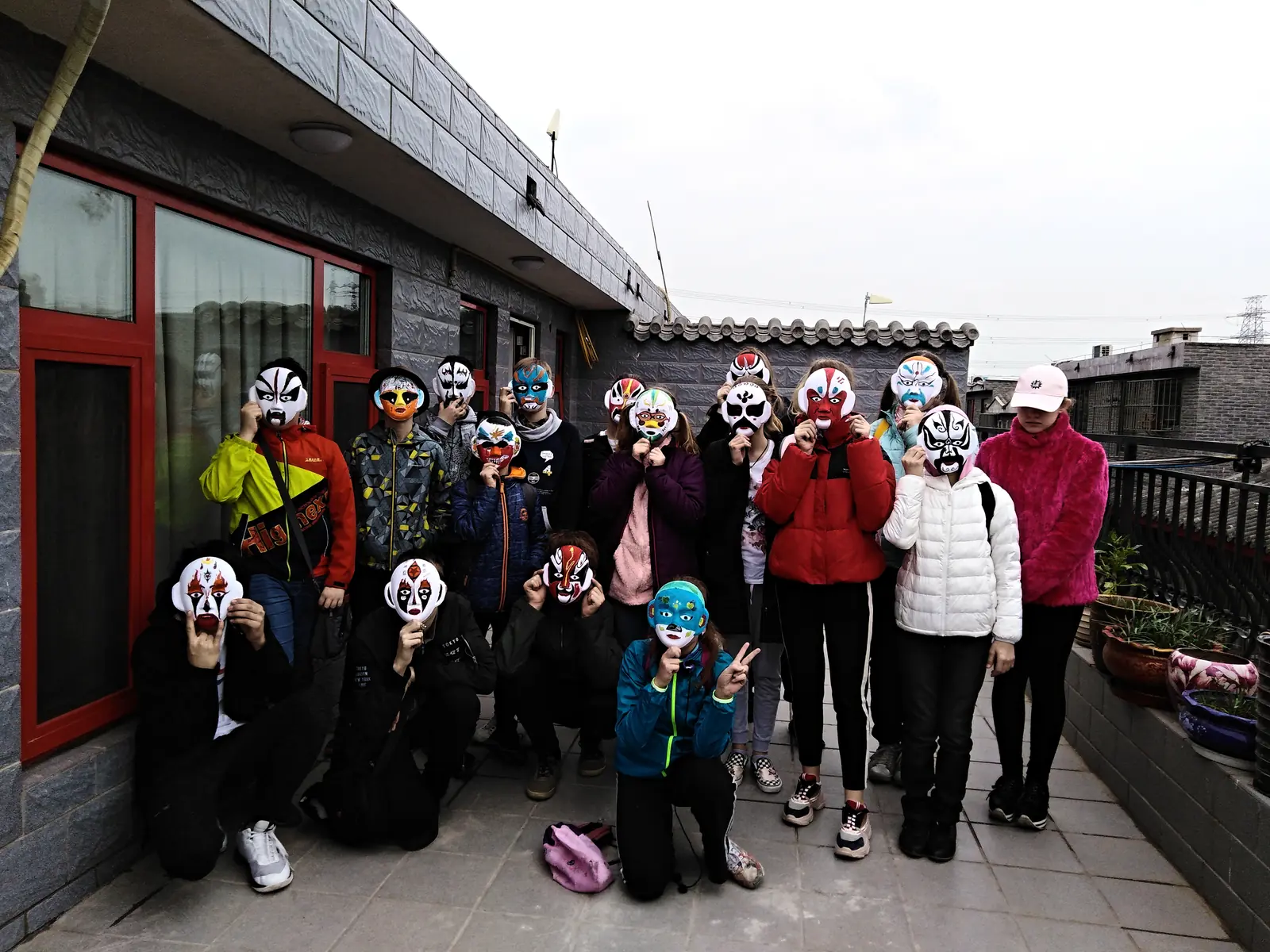 Students on a courtyard rooftop holding the Peking-opera masks they painted