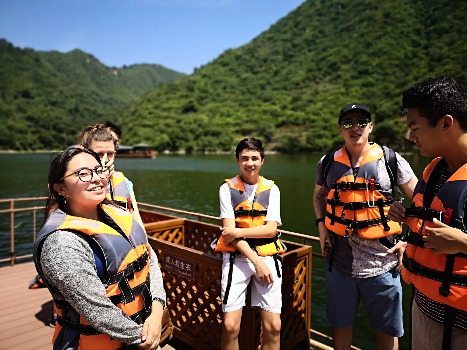 Campers in life jackets on a boat at a reservoir, green hills behind them