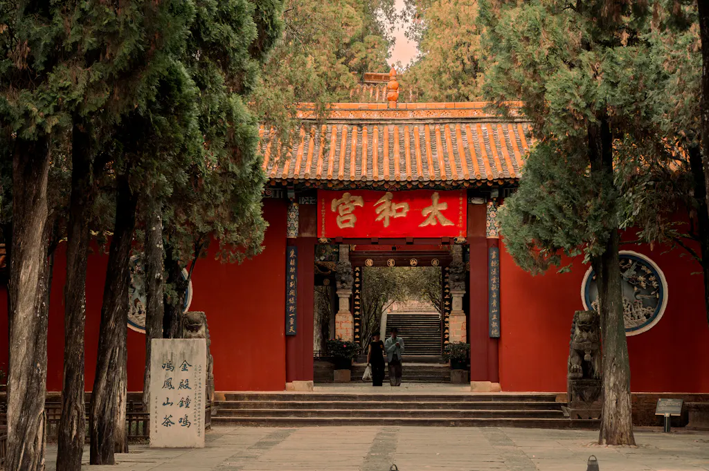 A vermillion temple gate under cypress trees in a Kunming park — stand-in for a photo of our students at Green Lake or the Stone Forest