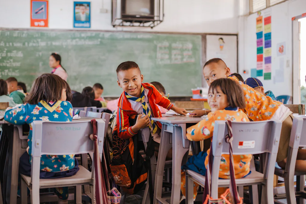 Young students at their desks in a bright classroom, one grinning over the back of his chair — stand-in for a photo of our own young classes