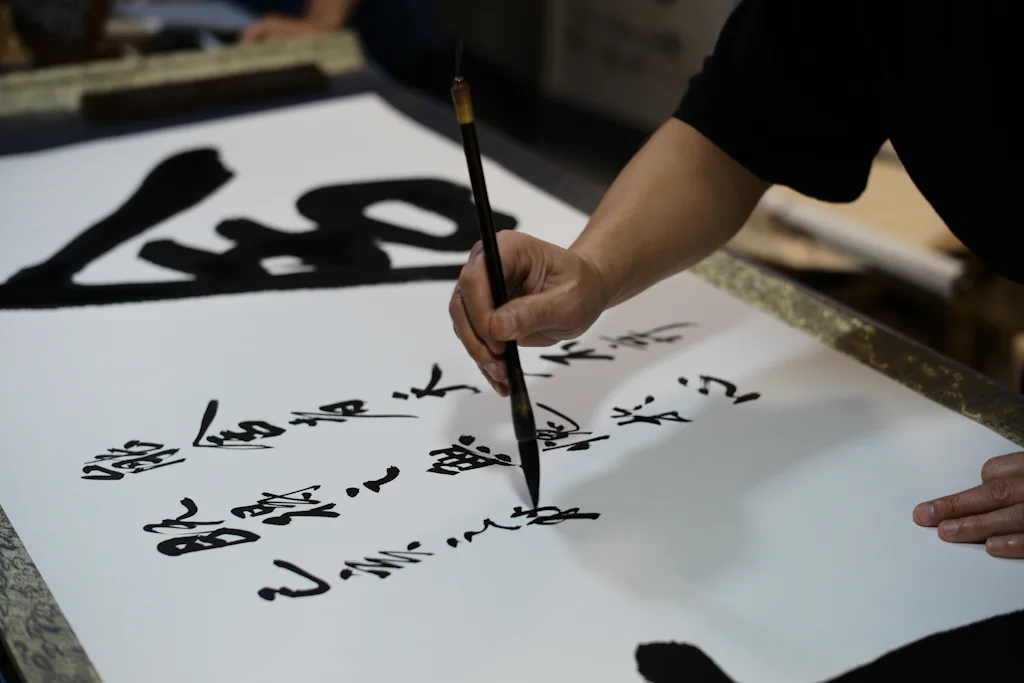 A calligrapher's hand drawing bold brush characters on white paper — stand-in for a photo of Ma Laoshi teaching at the Gaobeidian campus