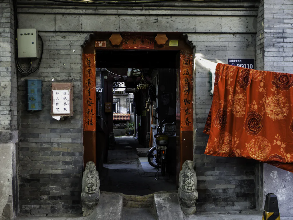 A grey-brick hutong doorway in Beijing, hung with a vermillion curtain and spring couplets — stand-in for a photo of the Gaobeidian campus gate